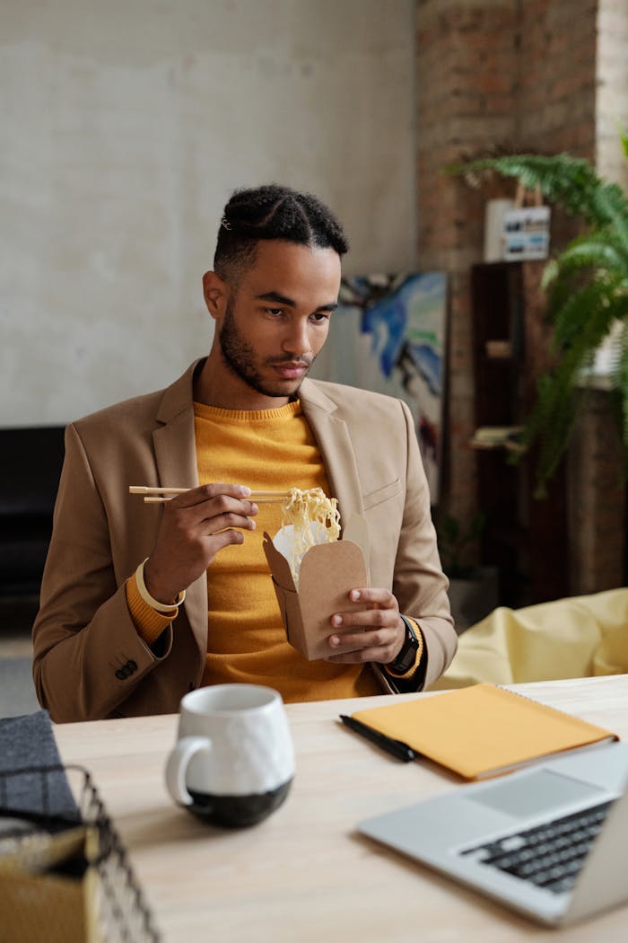 Man in Beige Blazer Eating Noodles in a Box